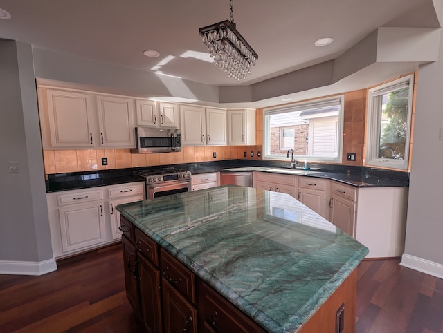 kitchen featuring a center island, decorative backsplash, appliances with stainless steel finishes, dark wood-style floors, and a sink