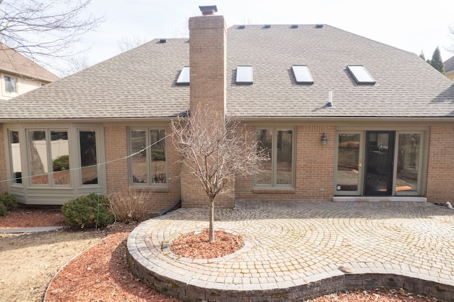 back of property with a patio area, brick siding, a chimney, and a shingled roof