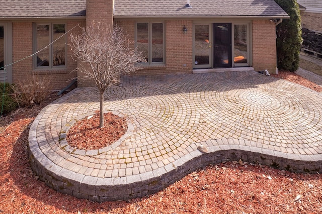 rear view of property featuring a patio area, brick siding, and roof with shingles