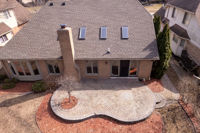 back of property with brick siding, roof with shingles, a chimney, and a patio area