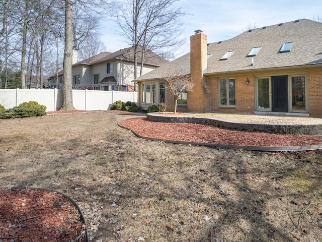 rear view of house featuring a patio, brick siding, a chimney, and fence