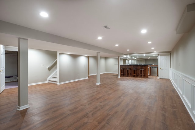 finished below grade area with wood finished floors, recessed lighting, a decorative wall, wet bar, and stairs