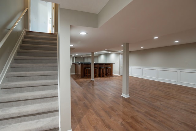 staircase with bar area, a wainscoted wall, recessed lighting, wood finished floors, and a decorative wall