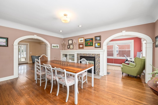 dining area featuring arched walkways, a stone fireplace, a healthy amount of sunlight, and light wood-type flooring