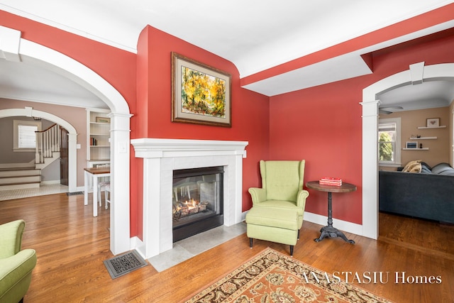 sitting room with visible vents, a fireplace with flush hearth, arched walkways, and wood finished floors