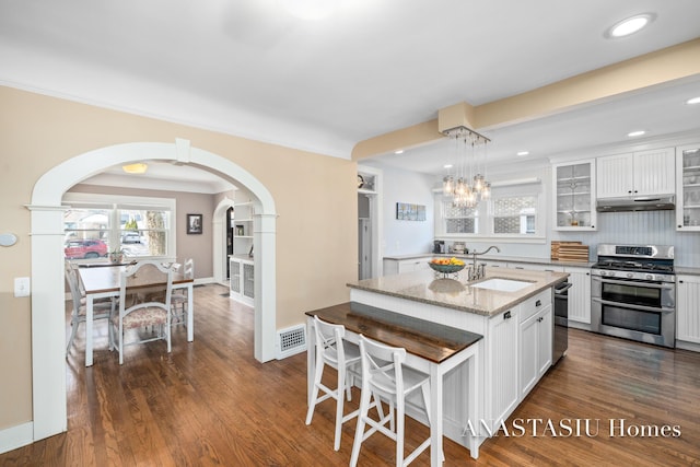 kitchen featuring double oven range, visible vents, arched walkways, a sink, and under cabinet range hood