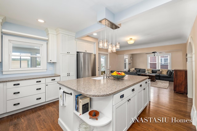 kitchen with a sink, dark wood finished floors, white cabinetry, freestanding refrigerator, and light stone countertops