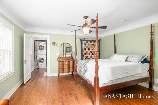 bedroom featuring ornamental molding, wood finished floors, stacked washer / drying machine, baseboards, and ceiling fan