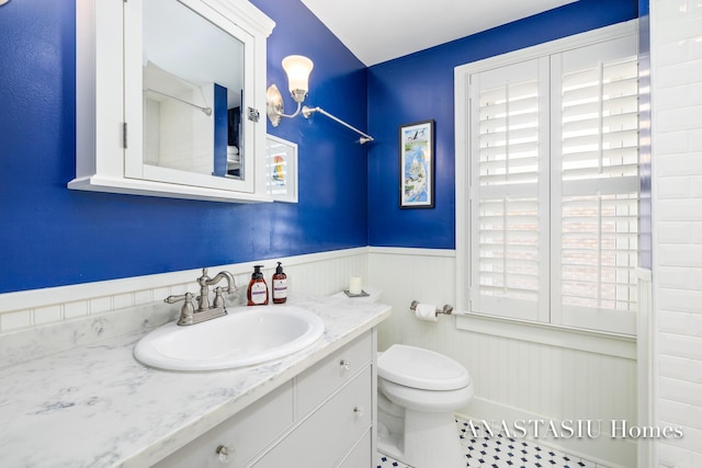 bathroom with a notable chandelier, a wainscoted wall, toilet, and vanity