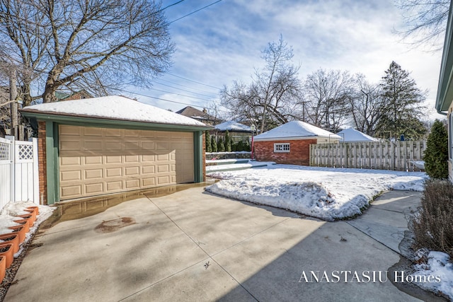 snow covered garage with a detached garage and fence