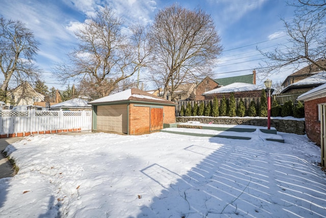 snow covered patio with an outbuilding, fence, and a detached garage