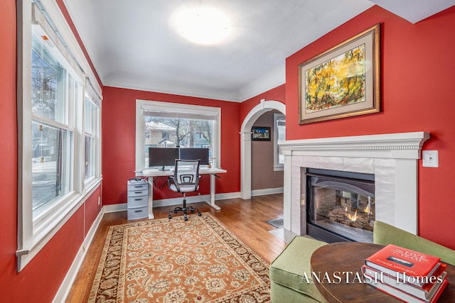 home office with arched walkways, a tile fireplace, baseboards, and wood finished floors