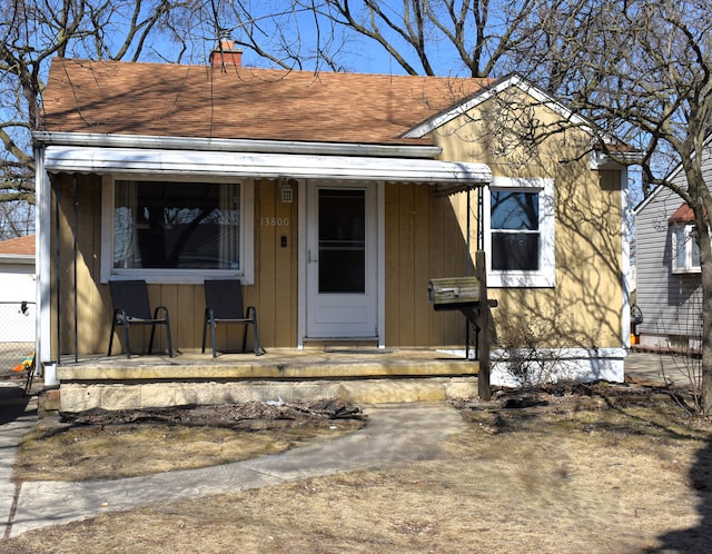 view of front facade with a chimney, covered porch, and a shingled roof