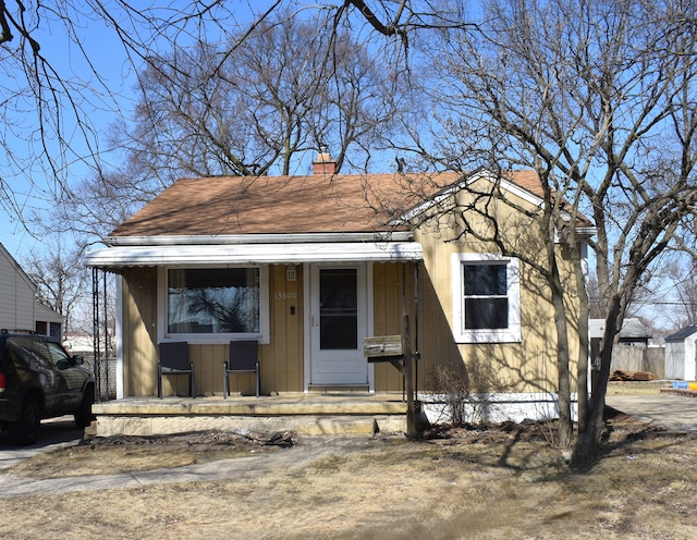 bungalow featuring covered porch, a chimney, and a shingled roof