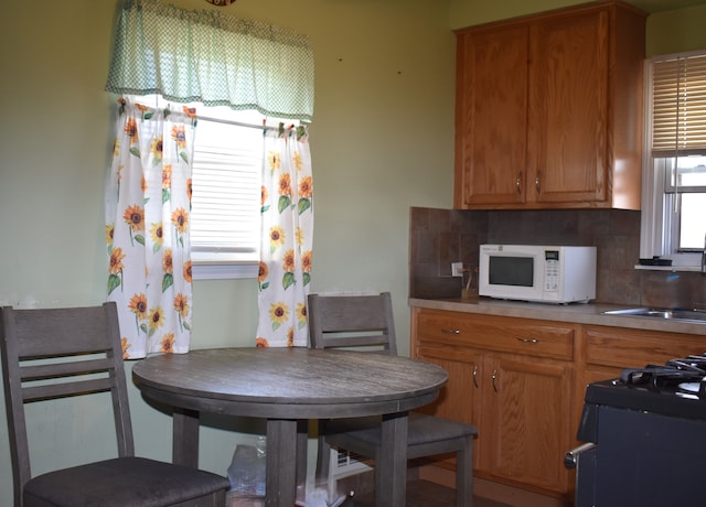 kitchen with white microwave, range with gas stovetop, tasteful backsplash, and a sink