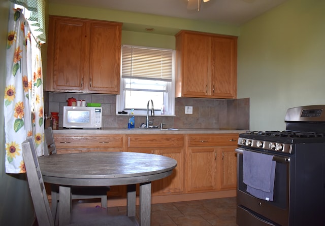 kitchen featuring a sink, decorative backsplash, white microwave, and stainless steel range with gas stovetop