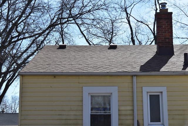 exterior details featuring a chimney and a shingled roof