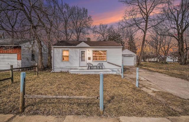 view of front facade featuring a detached garage, fence, concrete driveway, a chimney, and an outdoor structure