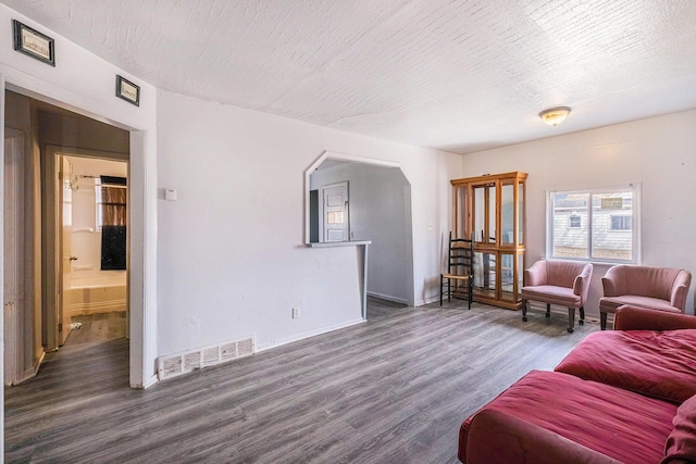 living room with visible vents, a textured ceiling, wood finished floors, arched walkways, and baseboards