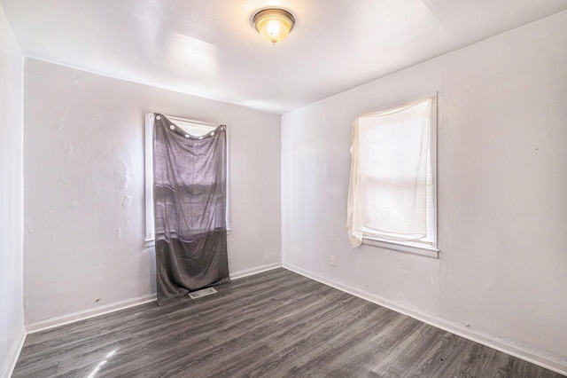 unfurnished room with dark wood finished floors, visible vents, and baseboards