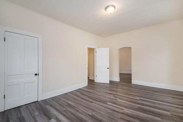 spare room with dark wood finished floors, baseboards, and arched walkways