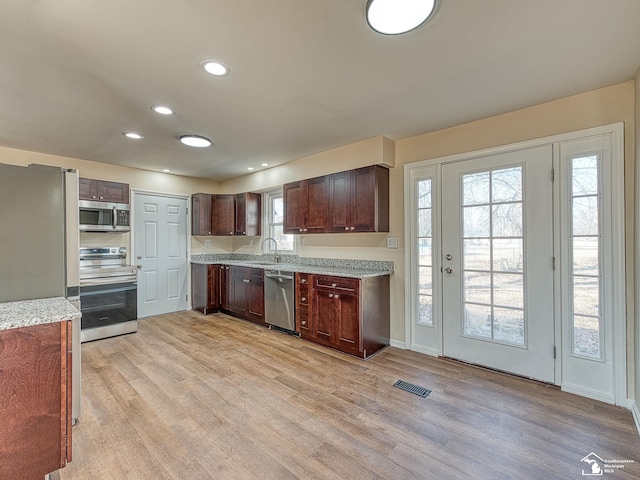 kitchen featuring visible vents, a sink, stainless steel appliances, dark brown cabinets, and light wood-style floors