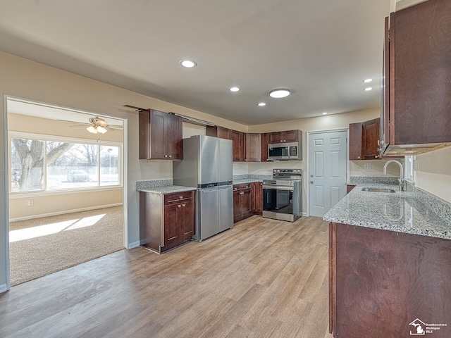 kitchen with baseboards, light stone counters, light wood-style floors, stainless steel appliances, and a sink