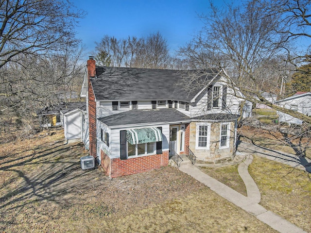 view of front of property featuring cooling unit, a chimney, a front lawn, and roof with shingles