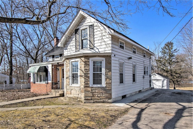 view of front of home featuring driveway, a chimney, an outdoor structure, stone siding, and a detached garage