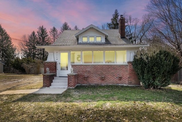 bungalow-style house with a yard, brick siding, and a chimney