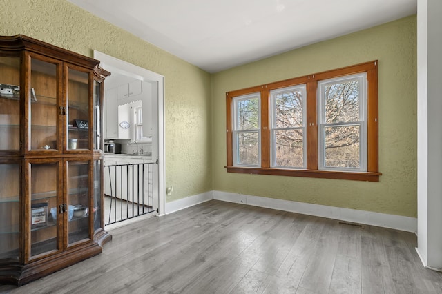 unfurnished dining area with visible vents, a sink, wood finished floors, baseboards, and a textured wall