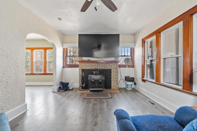 living room with visible vents, wood finished floors, baseboards, ceiling fan, and a textured wall