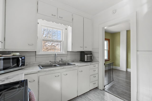 kitchen with stainless steel microwave, light countertops, range with electric stovetop, white cabinets, and a sink