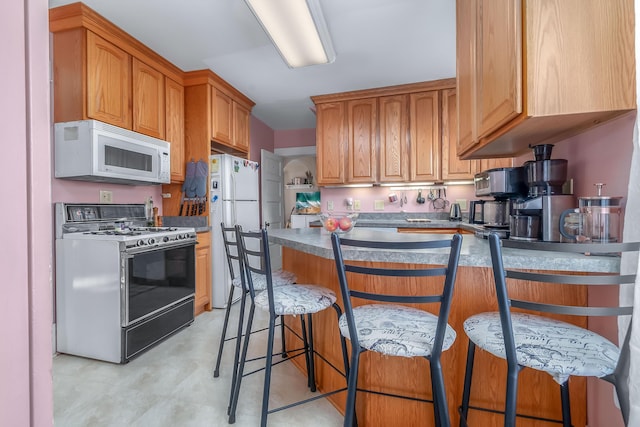 kitchen with white appliances, a peninsula, and a breakfast bar area