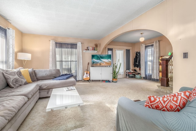 living area featuring vaulted ceiling, arched walkways, carpet floors, and a textured ceiling