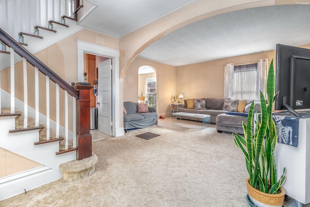 living room featuring stairs, carpet, arched walkways, and a textured ceiling