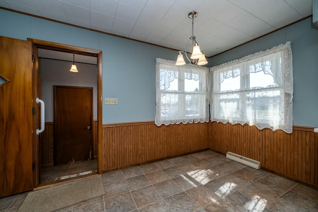 unfurnished dining area featuring wooden walls, a wainscoted wall, baseboard heating, and a chandelier