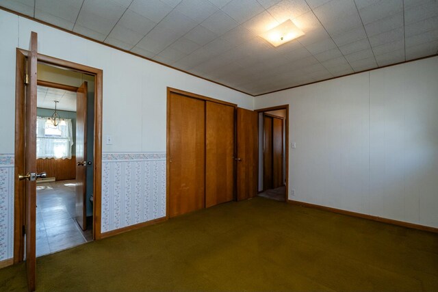 unfurnished bedroom with crown molding, carpet flooring, a closet, and a chandelier