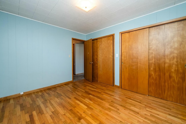 unfurnished bedroom featuring baseboards, multiple closets, and wood finished floors