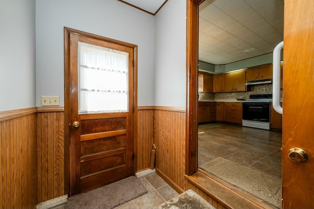 interior space with a wainscoted wall, range with electric cooktop, under cabinet range hood, wooden walls, and brown cabinetry