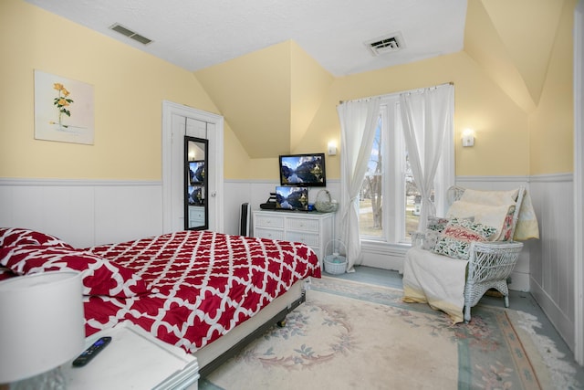 bedroom with vaulted ceiling, visible vents, a textured ceiling, and a wainscoted wall