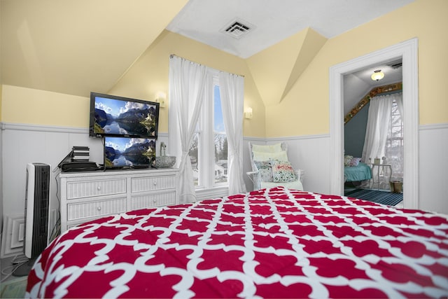 bedroom with visible vents, a wainscoted wall, and vaulted ceiling