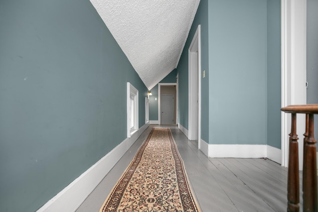 hallway with vaulted ceiling, a textured ceiling, baseboards, and wood finished floors