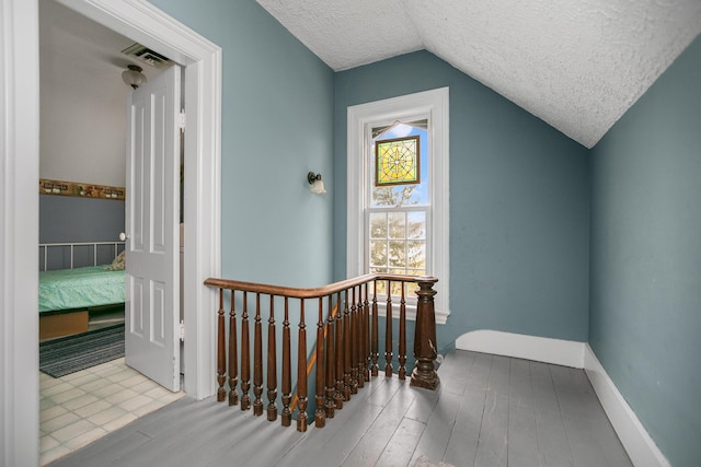 interior space with baseboards, lofted ceiling, an upstairs landing, wood finished floors, and a textured ceiling