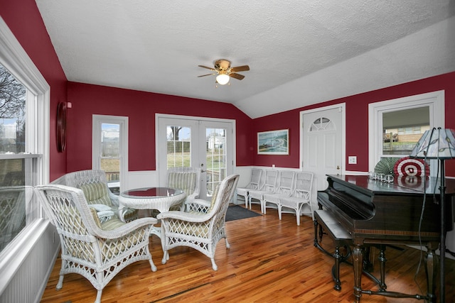 dining area with a wainscoted wall, vaulted ceiling, french doors, wood finished floors, and a ceiling fan