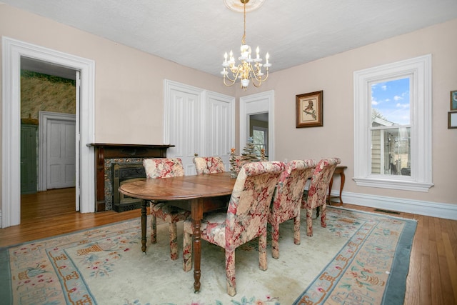 dining space with wood finished floors, visible vents, baseboards, an inviting chandelier, and a textured ceiling