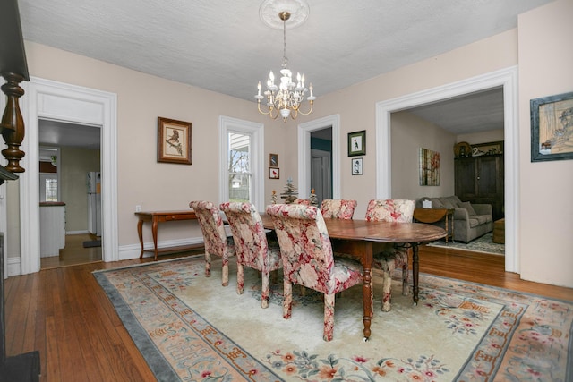 dining room featuring baseboards, wood-type flooring, a textured ceiling, and an inviting chandelier