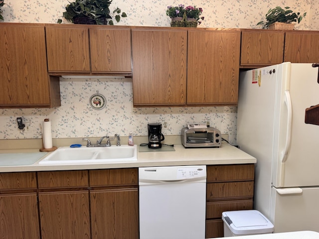 kitchen with a sink, white appliances, and wallpapered walls