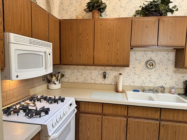 kitchen featuring a sink, white appliances, and wallpapered walls