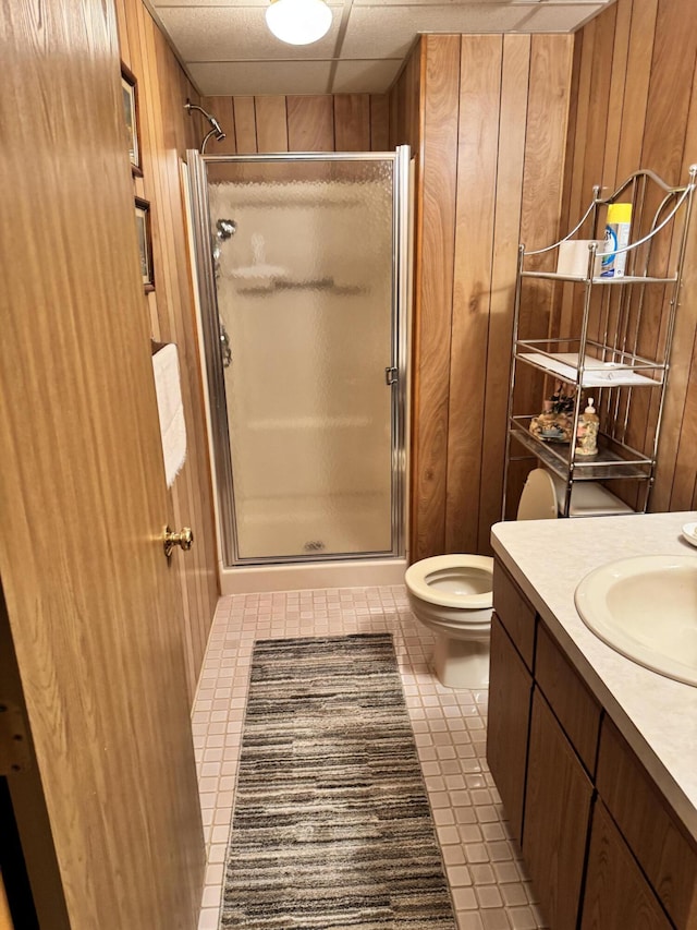 bathroom with vanity, toilet, a stall shower, and wood walls